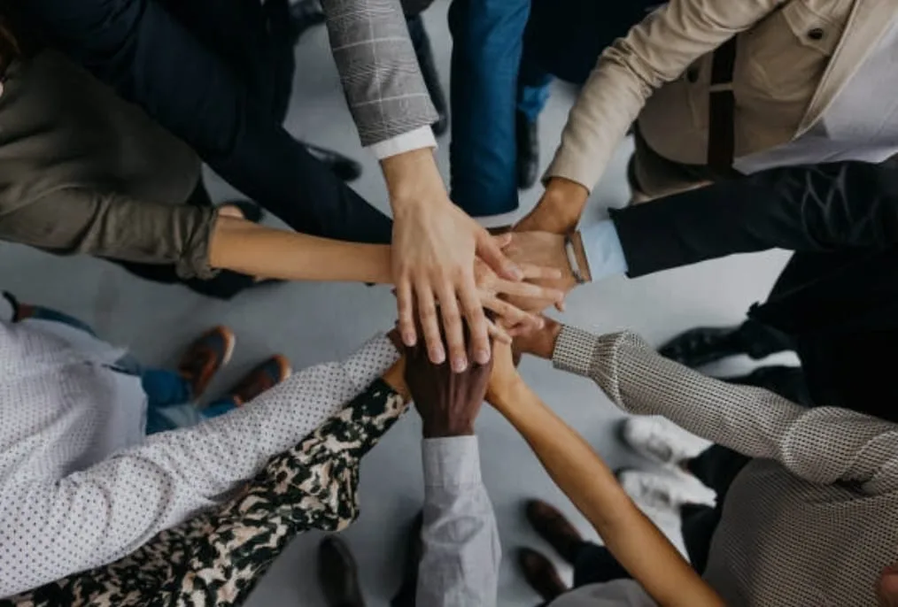 An overhead view of a diverse group of corporate professionals stacking their hands together in a huddle to show unity and teamwork. This collaborative visual highlights the student support network provided by a premier admission consultancy for MBBS, B.Tech, BDS, BPT, B.Pharm, LLB, B.Ed, and many more graduation, post graduation, and diploma courses across India and abroad.